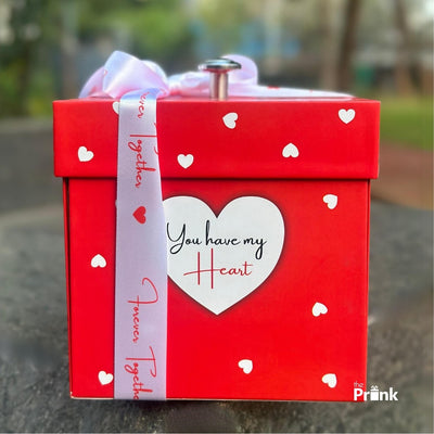 A red gift box adorned with small white hearts and a white heart on the front reading 