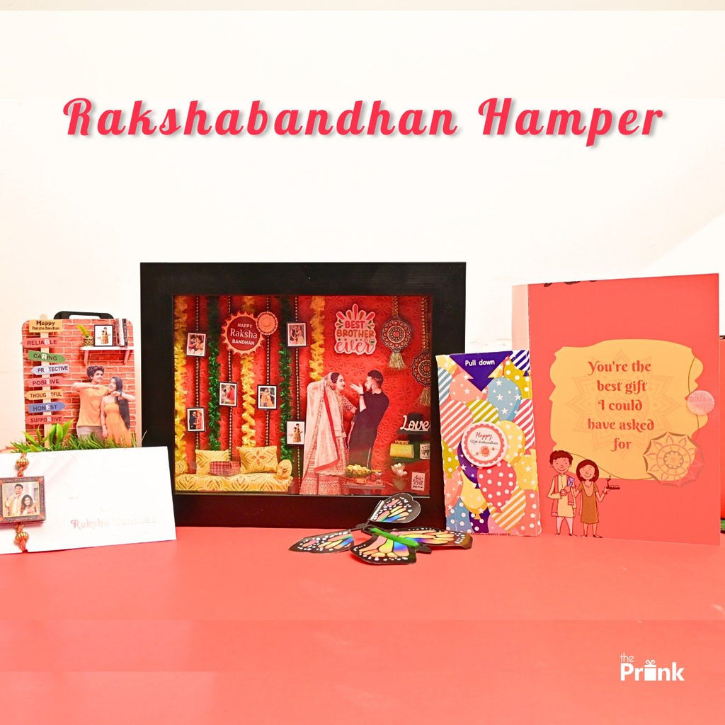 Rakshabandhan gift set on a red surface, featuring a festive frame, butterfly card, decorative magnet and a rakhi card.. Text reads "Rakshabandhan Hamper."