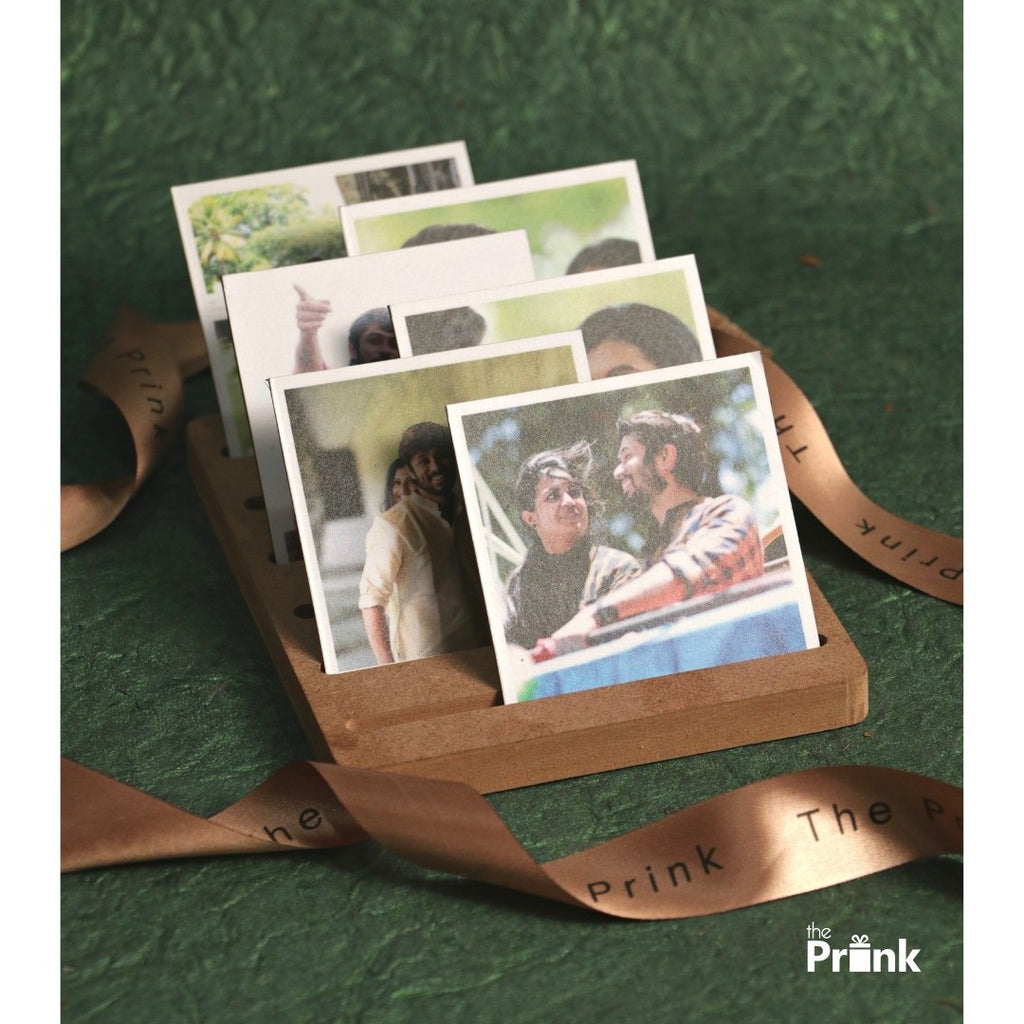 A wooden photo holder displays three square photo magnets in a row, each showing people in cheerful, candid moments. The background is a textured green surface.
