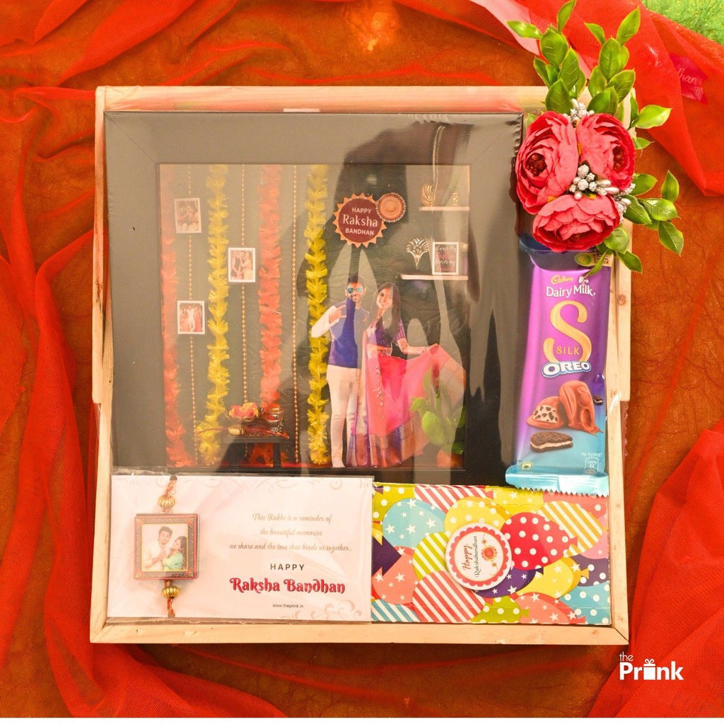 Gift box for Raksha Bandhan with a decorated card, chocolate, floral embellishments, and a personal photo frame. Vibrant and festive theme.