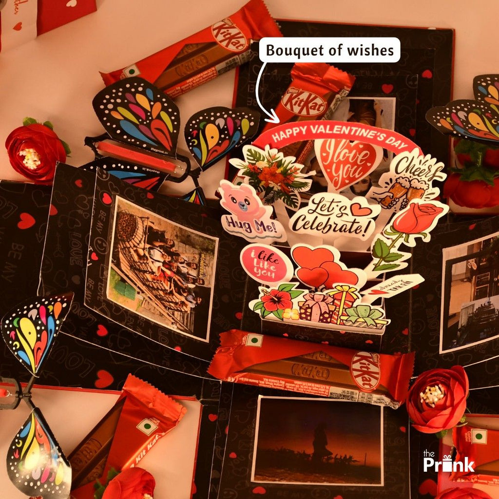 Valentine's Day-themed explosion box with chocolates, vibrant butterfly cutouts, red roses, photos, and festive stickers with loving messages.