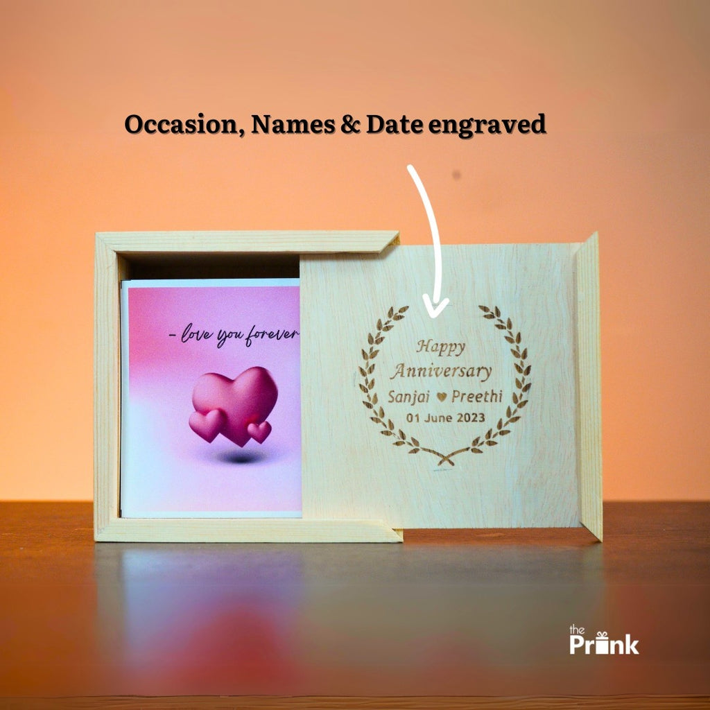 A wooden sliding box engraved with "Happy Anniversary" and names and date on the right. On the left, a card with pink hearts and "love you forever."