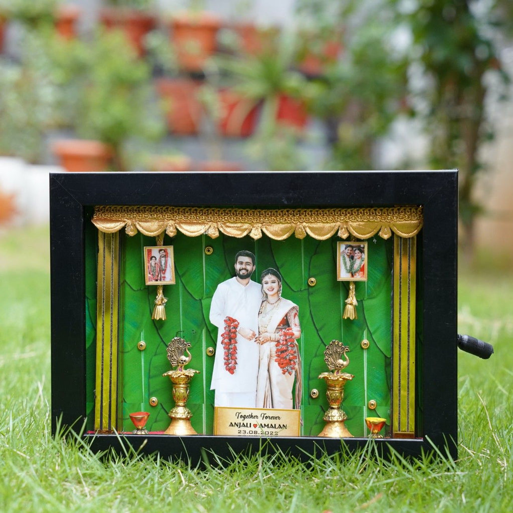 Framed 3D wedding collage with a smiling couple in white attire, adorned with red garlands. Gold decor on a vibrant green background. Elegant and celebratory.