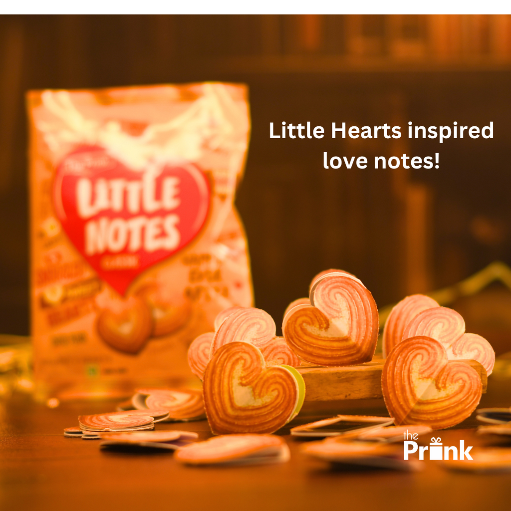 Heart-shaped notes displayed on a wooden surface, with a blurred package in the background. Text reads "Little Hearts inspired love notes!" Warm tone.