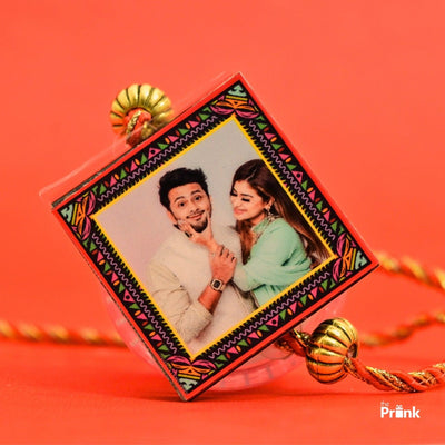 A colorful rakhi against an orange background, featuring a playful smiling siblings in traditional attire within a decorative frame.