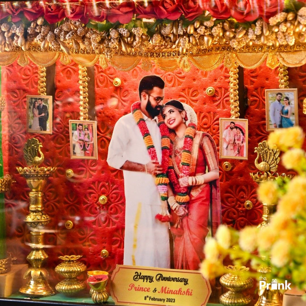 Happy anniversary frame featuring a couple in festive attire with garlands, surrounded by ornate golden decor and small photos, conveying joy and celebration.
