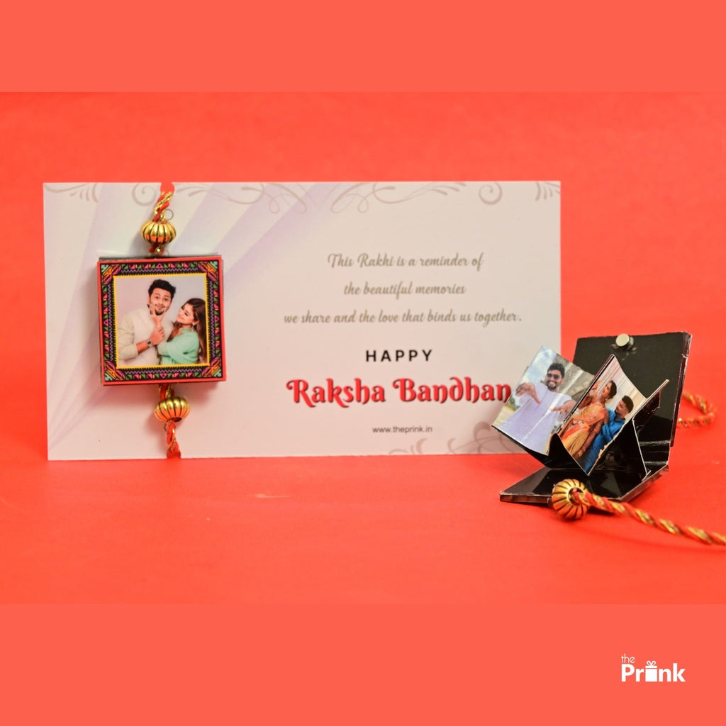 A Raksha Bandhan card with a colorful rakhi beside it on a red background. The card wishes "Happy Raksha Bandhan" with personal photos attached.