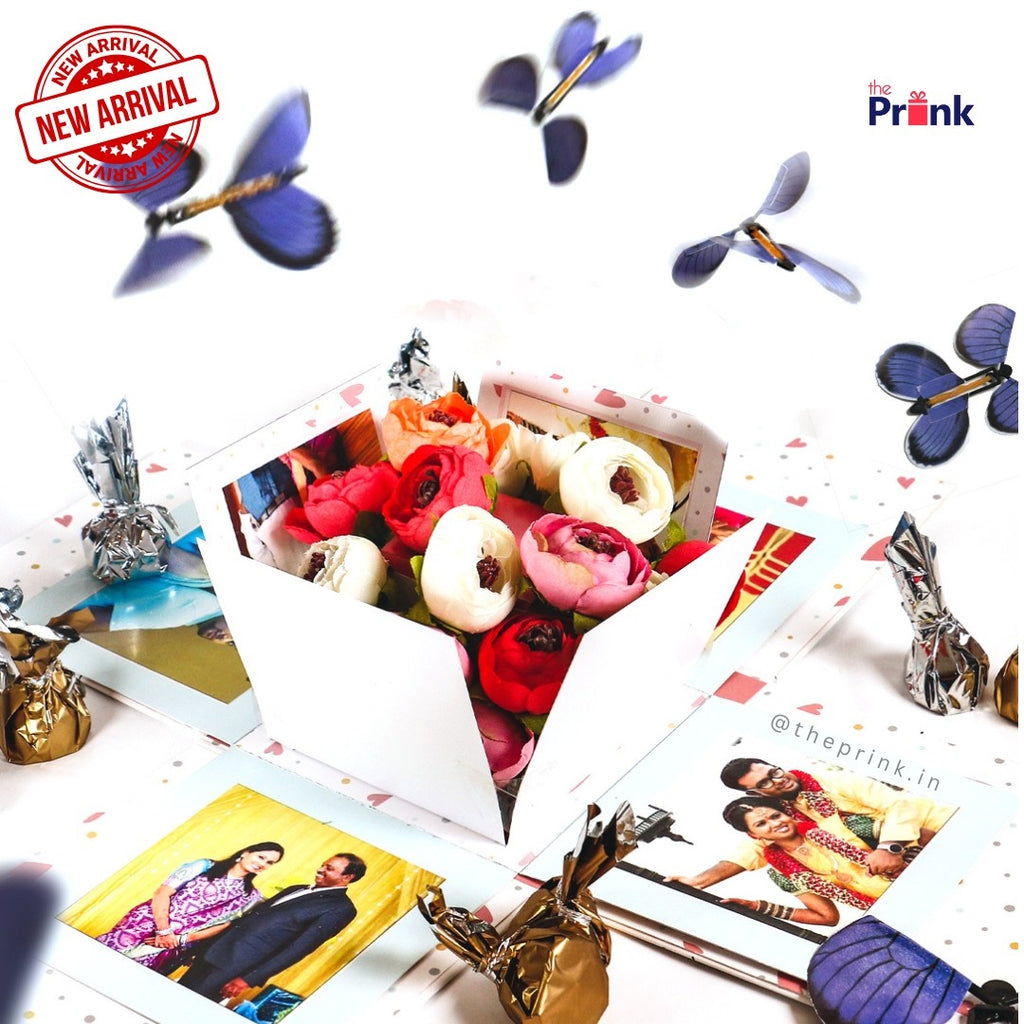 Gift box with vibrant roses surrounded by blue butterflies and wrapped chocolates. Includes photo prints. New arrival stamp adds excitement.