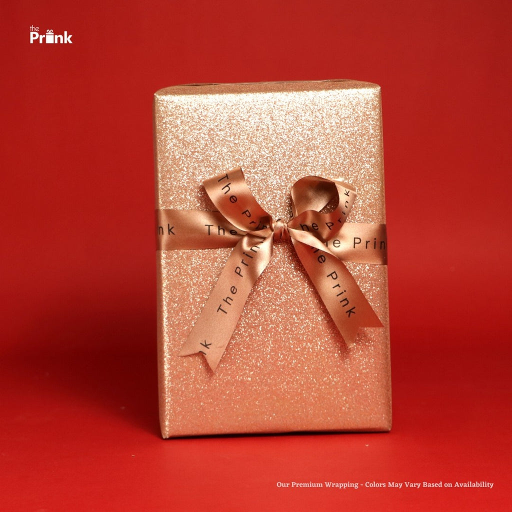A glittering gold gift box wrapped with a satin ribbon featuring the text "The Prink" on it, set against a vibrant red background.