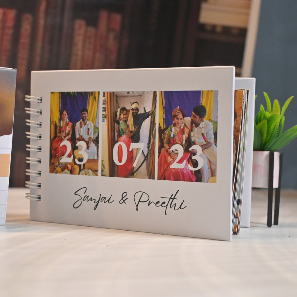 A photo album with three wedding pictures marked "23 07 23," featuring a couple in traditional attire, titled "Sanjai & Preethi," on a table near a plant.
