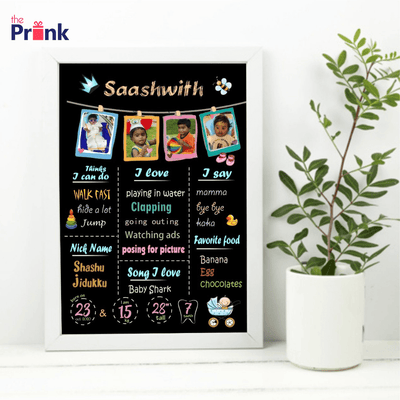 Framed child milestone poster with colorful graphics and baby photos, listing activities, favorites, and first words. A plant is beside it.