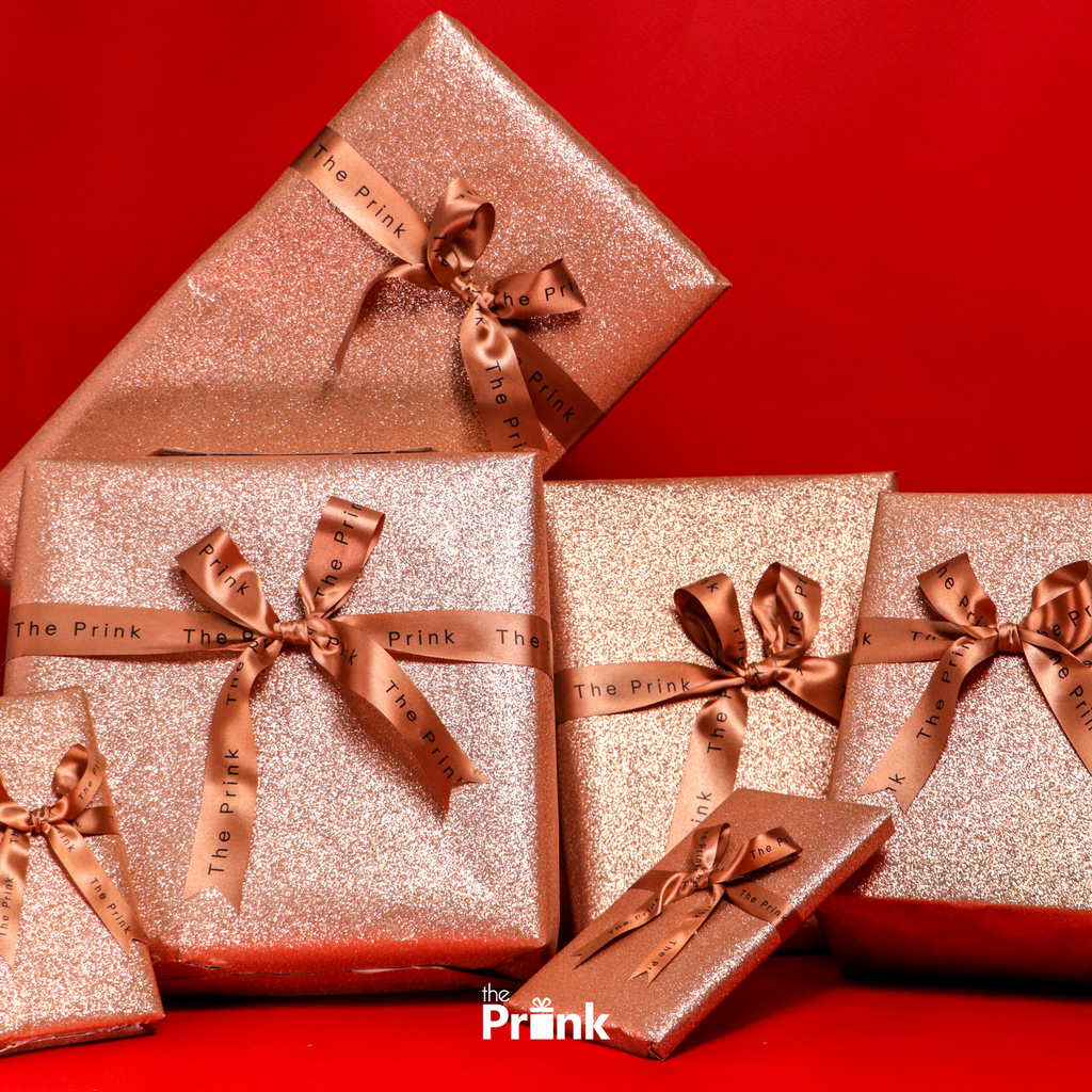 A stack of glittering, rose gold gift boxes tied with satin bows on a vibrant red background, conveying an elegant and festive atmosphere.