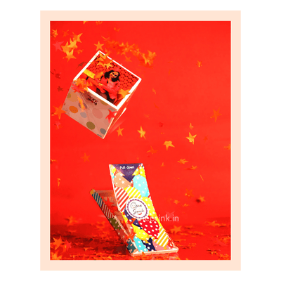 Colorful gift box against a vibrant red background, surrounded by floating confetti & stars. The box features playful patterns and a 